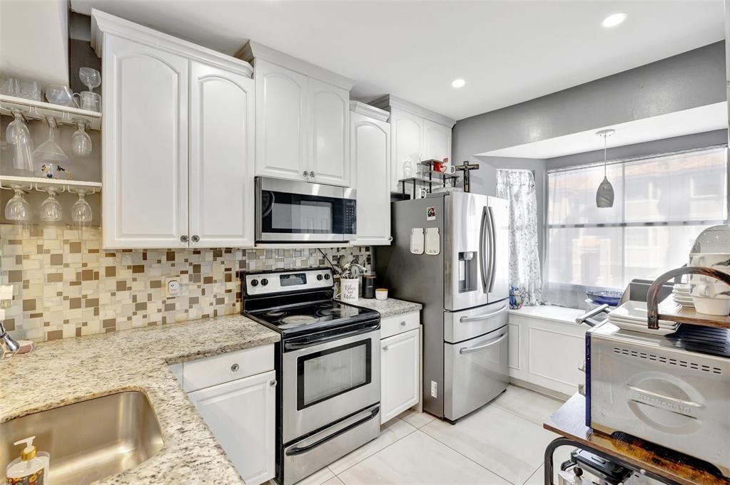 A kitchen features white cabinets, stainless steel appliances, granite countertops, and a mosaic tile backsplash — 12662 NW 14TH STREET, SUNRISE, FL