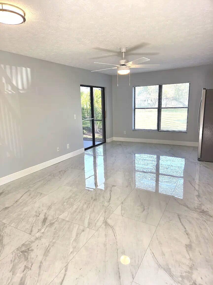 An empty room features gray walls, a ceiling fan, and polished white marble-look tile flooring — 6551 SE Federal Highway # 104, Stuart FL 34997, STUART, FL