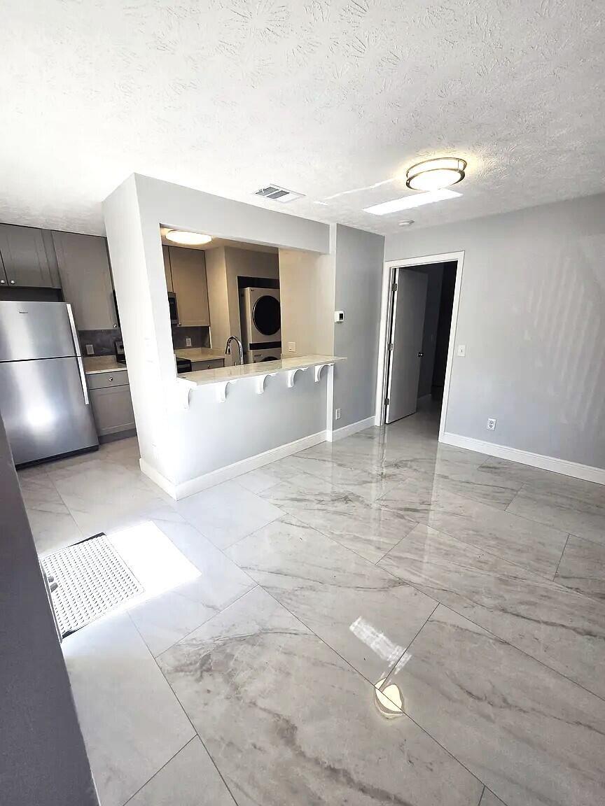 A kitchen with a breakfast bar overlooks a living area with light-colored marble-look tile flooring — 6551 SE Federal Highway # 104, Stuart FL 34997, STUART, FL