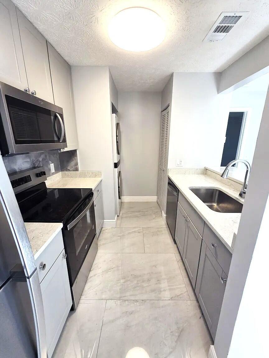 A galley kitchen features gray cabinets, stainless steel appliances, and light-colored tile flooring — 6551 SE Federal Highway # 104, Stuart FL 34997, STUART, FL