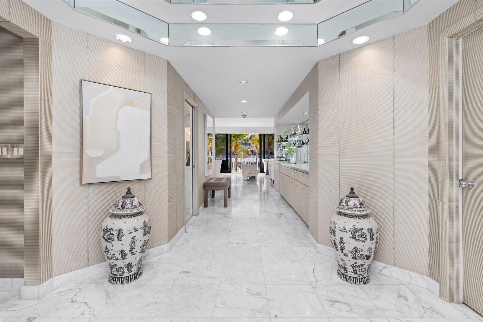 A marble-floored hallway features two large decorative urns, textured wall panels, and a mirrored ceiling — 2000 S Ocean Boulevard # 107n, Palm Beach FL 33480, PALM BEACH, FL