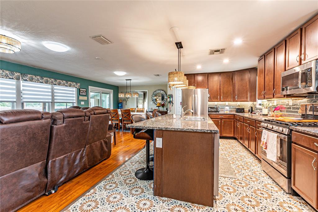 A kitchen with granite countertops, wood cabinets, and patterned tile flooring opens to a living area — 5233 HILL DRIVE, ZEPHYRHILLS, FL