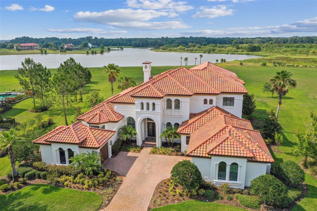 An aerial view of a two-story Mediterranean-style house with a red tile roof near water — 12310 STONELAKE RANCH BOULEVARD, THONOTOSASSA, FL