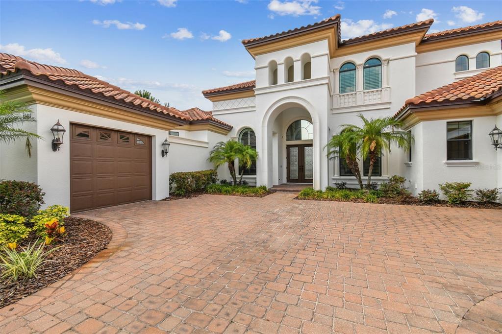 A two-story Mediterranean-style house features a paver driveway, a brown garage door, and arched windows — 12310 STONELAKE RANCH BOULEVARD, THONOTOSASSA, FL
