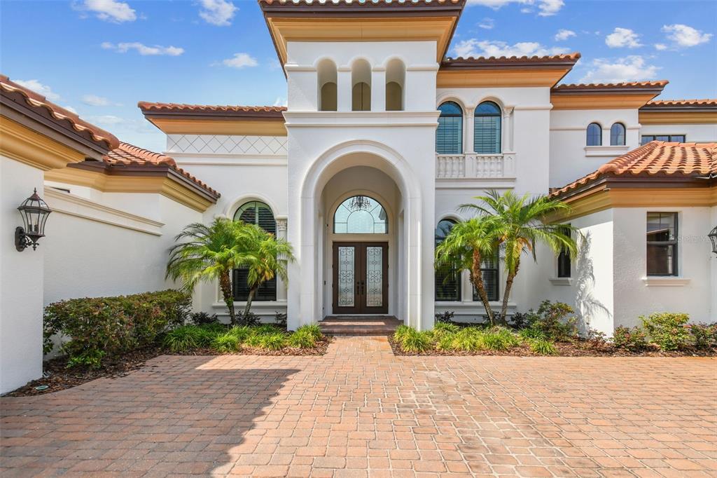 A Mediterranean-style house exterior features a brick paver driveway, arched entryway, and terracotta roof tiles — 12310 STONELAKE RANCH BOULEVARD, THONOTOSASSA, FL
