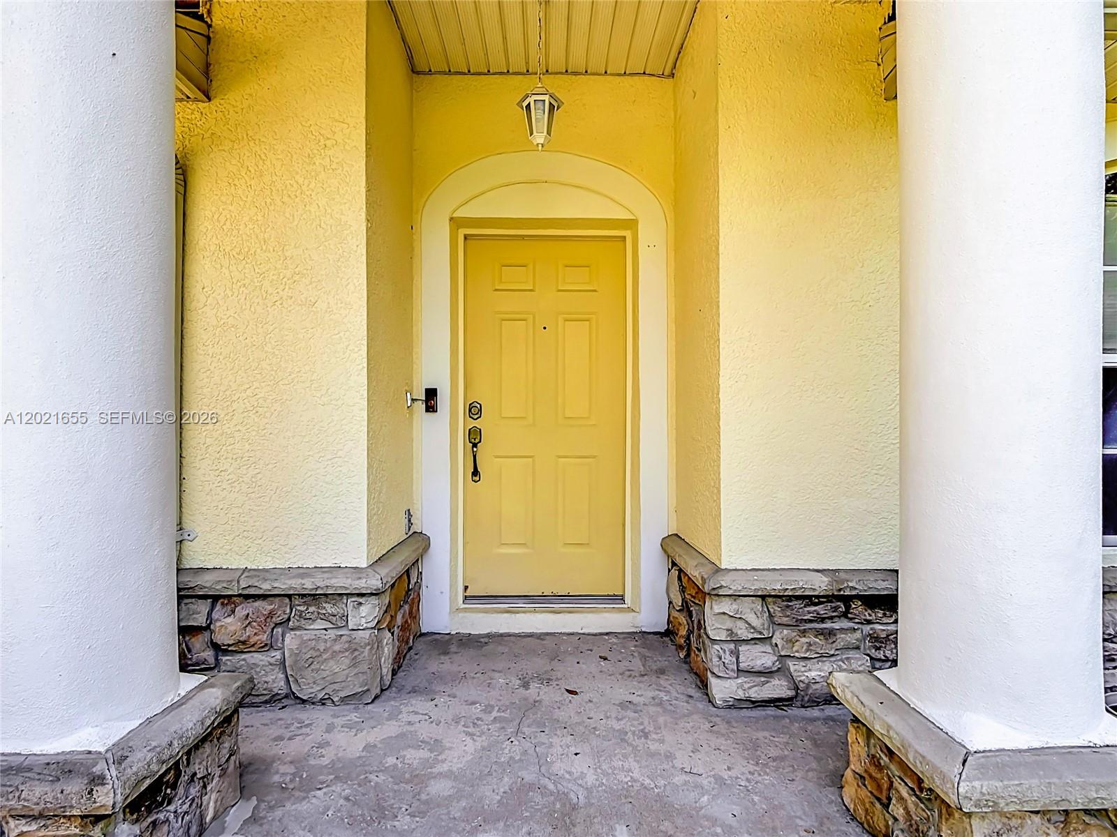 A yellow front door is framed by stone-based walls and two large white columns — 2917 Evans Way, Kissimmee FL 34758, KISSIMMEE, FL