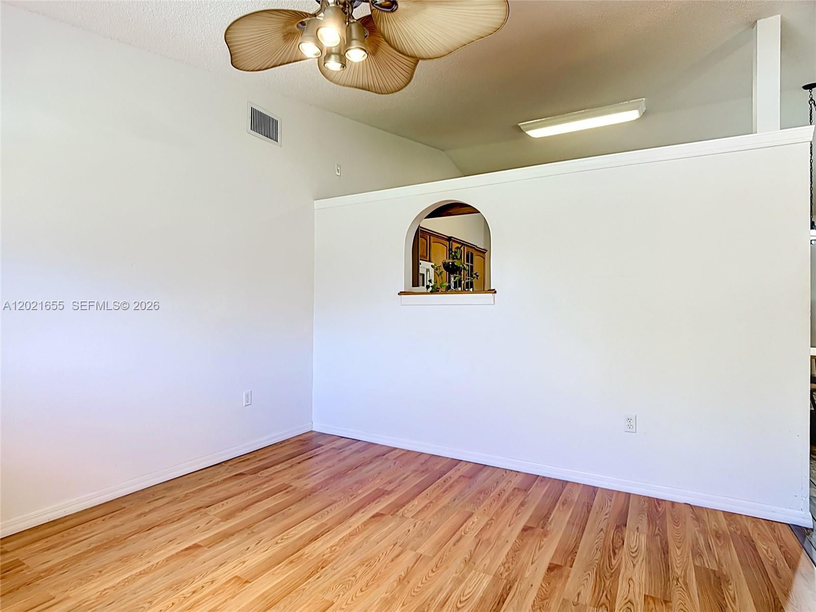 An empty room features wood-look flooring, a ceiling fan, and a wall with an arched cutout — 2917 Evans Way, Kissimmee FL 34758, KISSIMMEE, FL