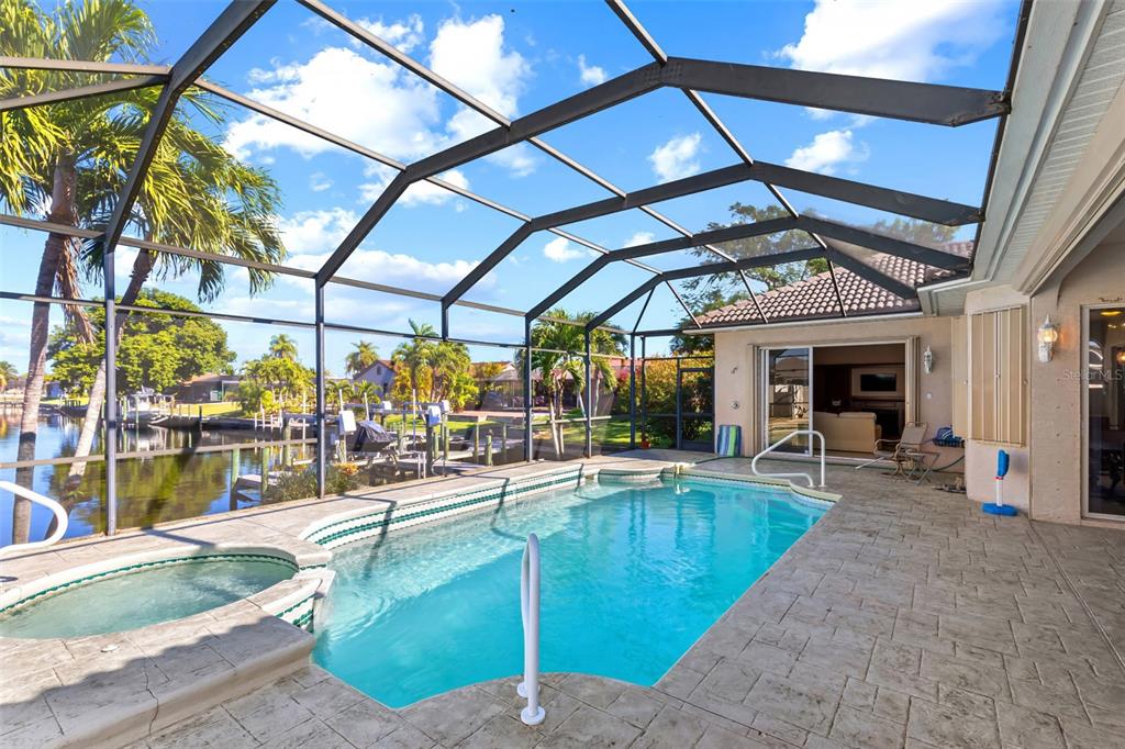 A screened-in patio features a swimming pool, a hot tub, and a view of a canal — 1935 SE 26TH STREET, CAPE CORAL, FL