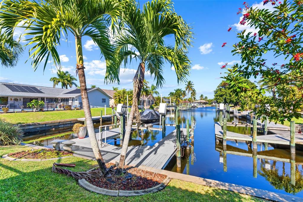 A canal view featuring a wooden boat dock, palm trees, and a house with solar panels — 1935 SE 26TH STREET, CAPE CORAL, FL