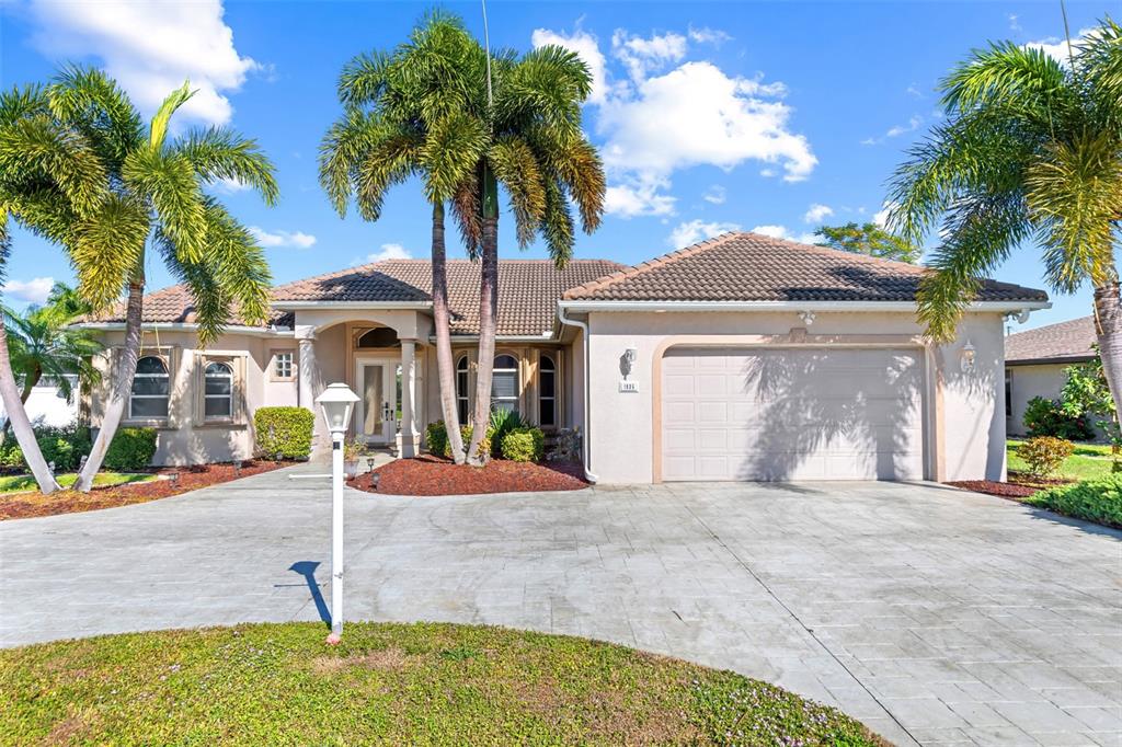 A single-story house with a beige stucco exterior, a tiled roof, and a paved driveway — 1935 SE 26TH STREET, CAPE CORAL, FL