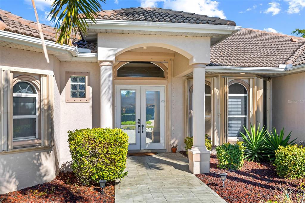 The exterior of a house features a tiled roof, arched entryway, and double glass doors — 1935 SE 26TH STREET, CAPE CORAL, FL