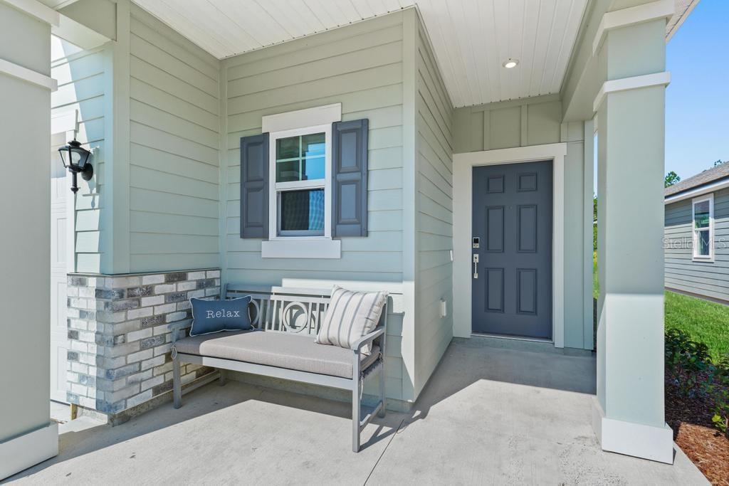 A light green house exterior features a covered porch with a bench and gray door — 1343 RIBBON PLACE, PALM COAST, FL