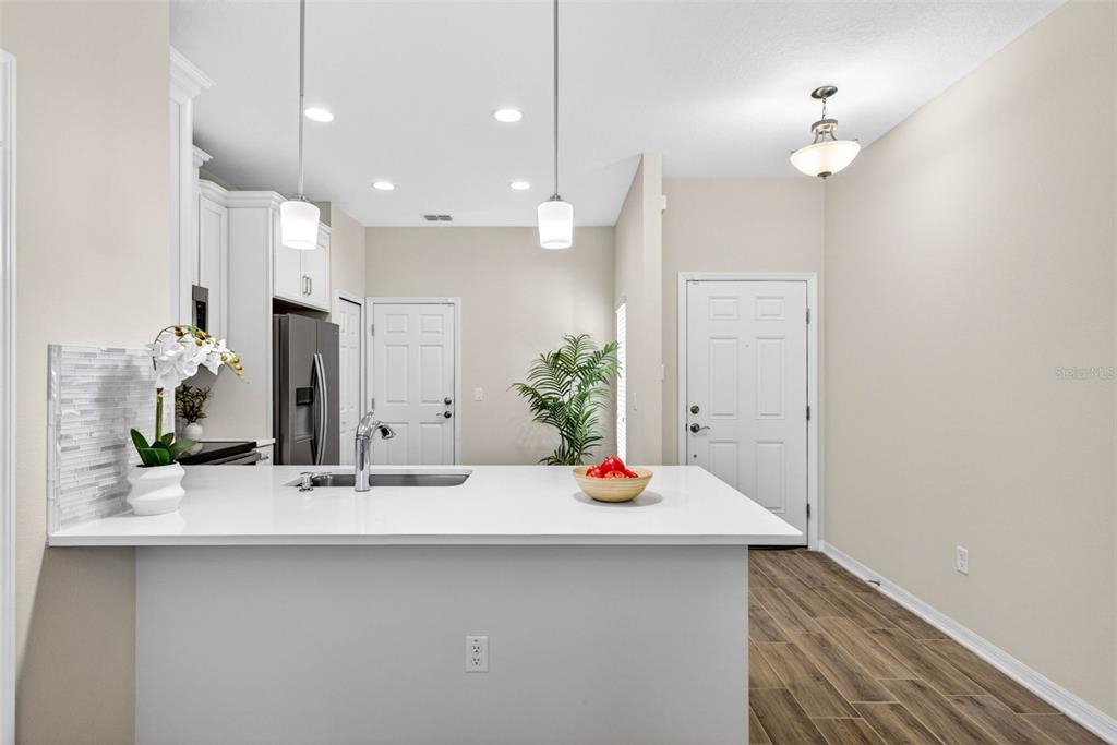 A kitchen features a white quartz island with a sink, pendant lighting, and wood-look flooring — 2464 STAPLEFORD PLACE, WESLEY CHAPEL, FL