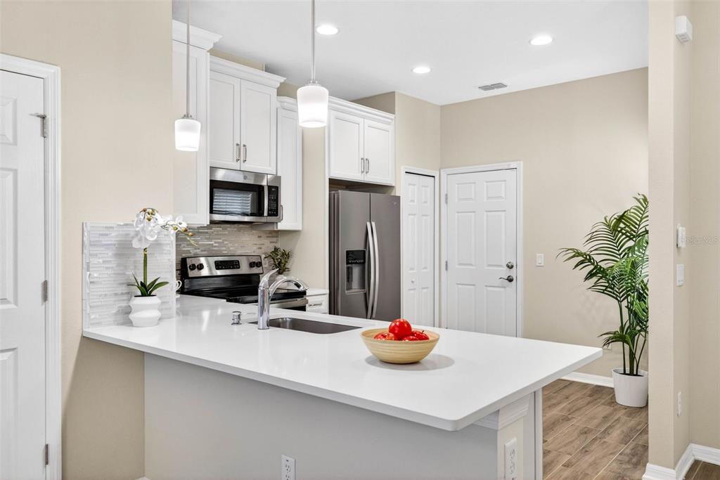A kitchen features white cabinets, stainless steel appliances, a quartz countertop, and a breakfast bar — 2464 STAPLEFORD PLACE, WESLEY CHAPEL, FL