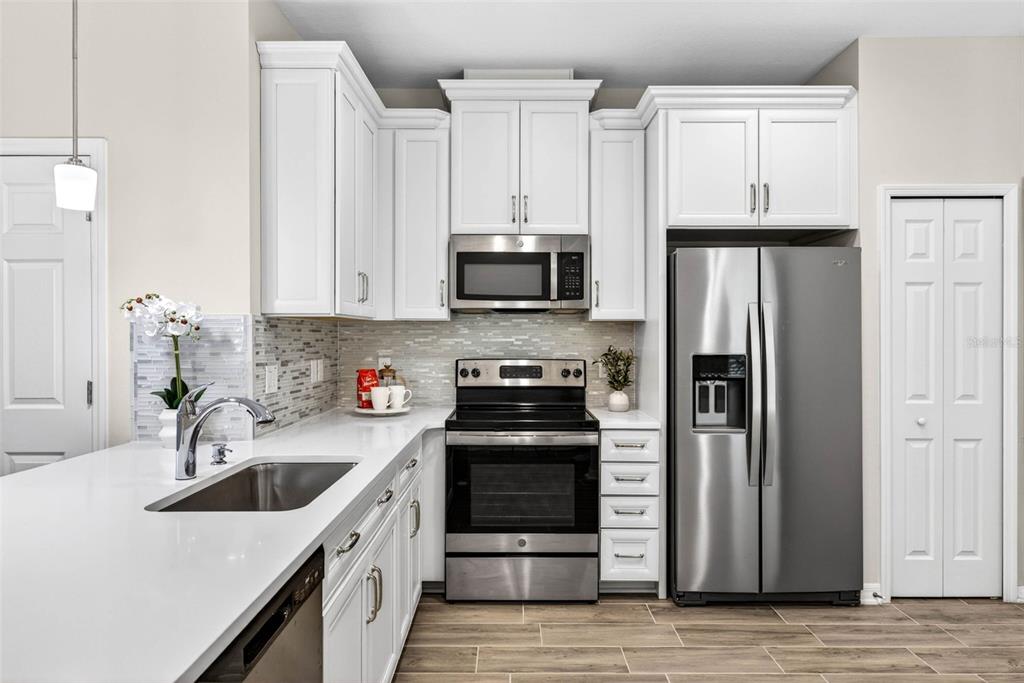 A kitchen features white cabinets, stainless steel appliances, a quartz countertop, and a tiled backsplash — 2464 STAPLEFORD PLACE, WESLEY CHAPEL, FL