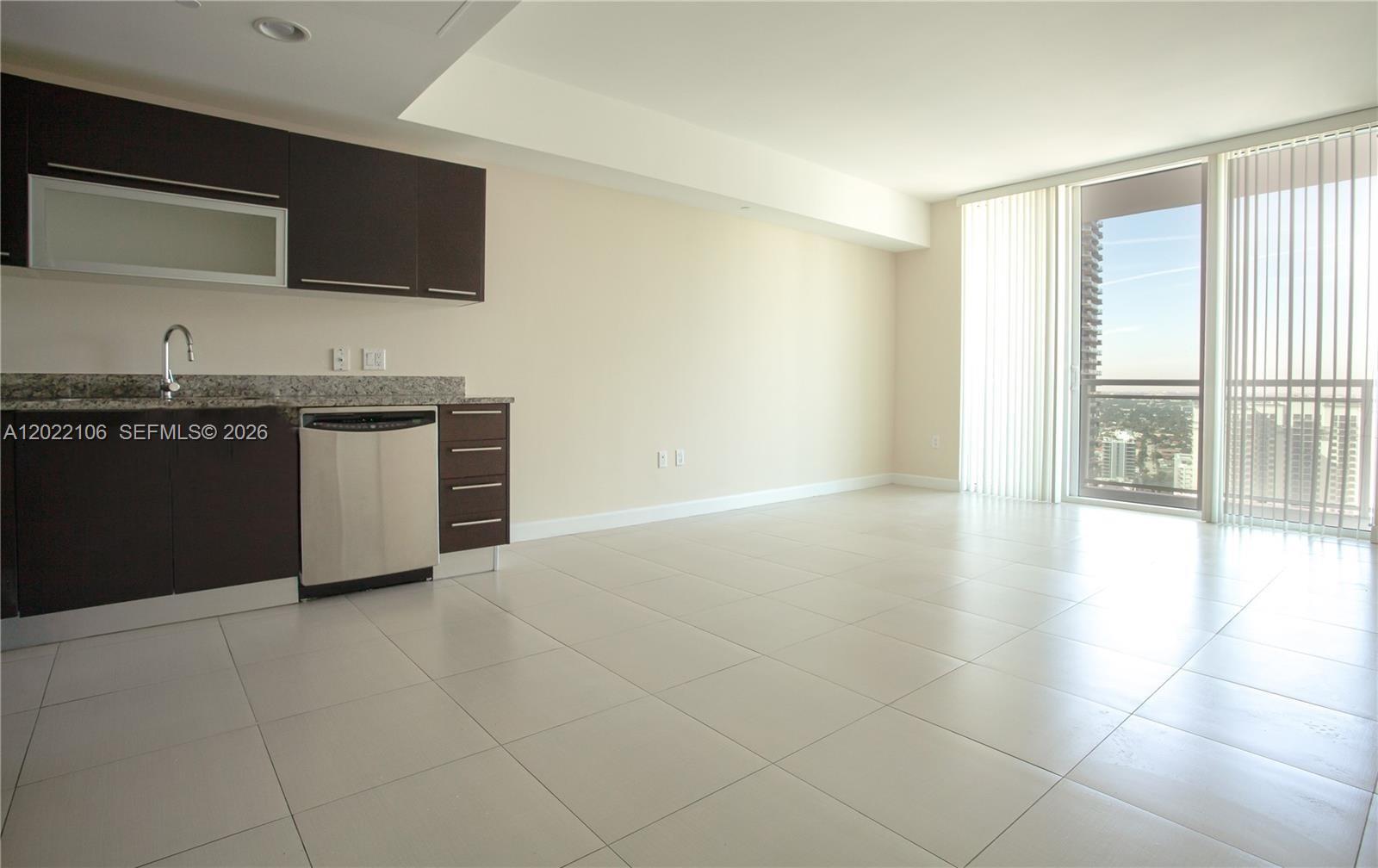 A modern kitchen with dark cabinets and stainless steel appliances opens into a tiled living area — 951 Brickell Ave # 4009, Miami FL 33131, MIAMI, FL
