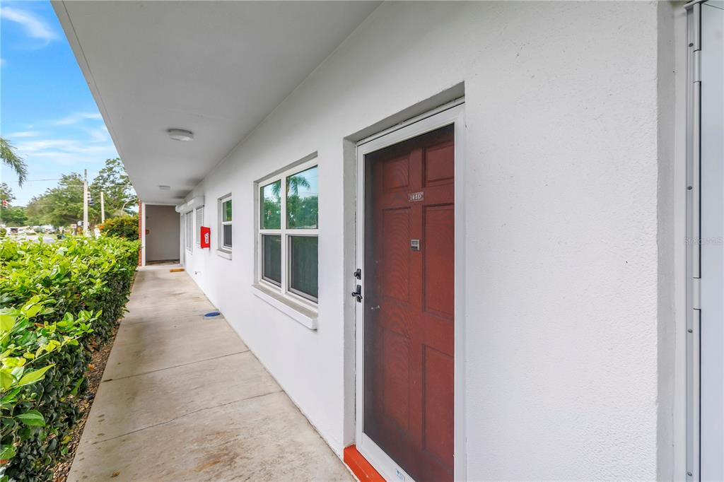 A white exterior walkway leads to a red front door with a screen door — 5729 13TH AVENUE N UNIT 102D, ST PETERSBURG, FL