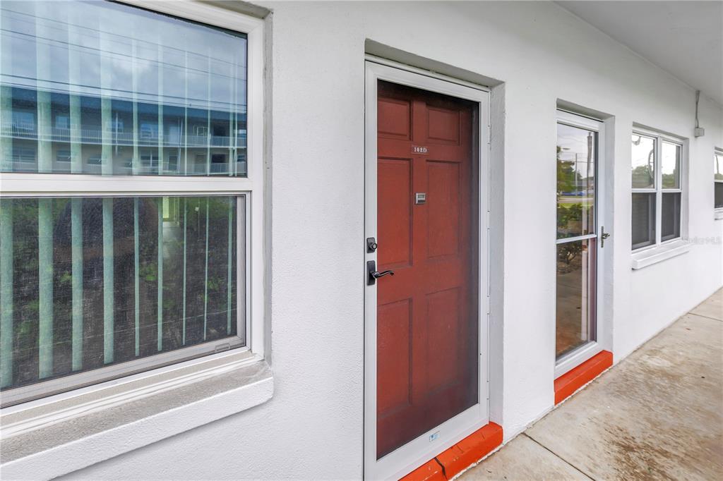 A red front door with a screen door sits on a white exterior walkway — 5729 13TH AVENUE N UNIT 102D, ST PETERSBURG, FL