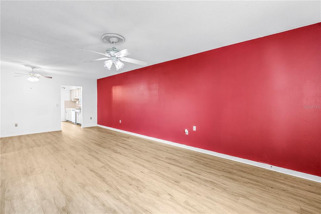 A spacious room features light wood-look flooring, white walls, and a prominent red accent wall — 5729 13TH AVENUE N UNIT 102D, ST PETERSBURG, FL
