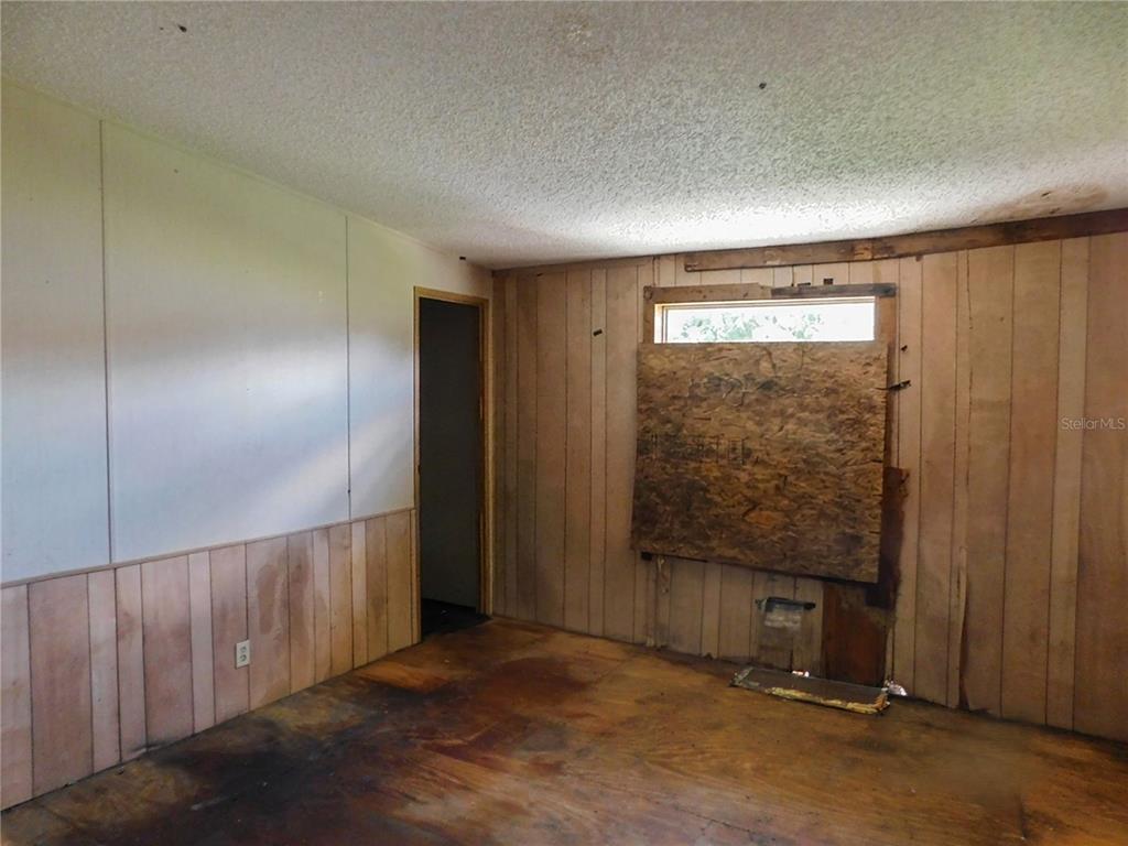 An interior room features wood-paneled walls, a plywood-covered window, and exposed subflooring — 2634 SEA OATS CIRCLE N, LAKELAND, FL