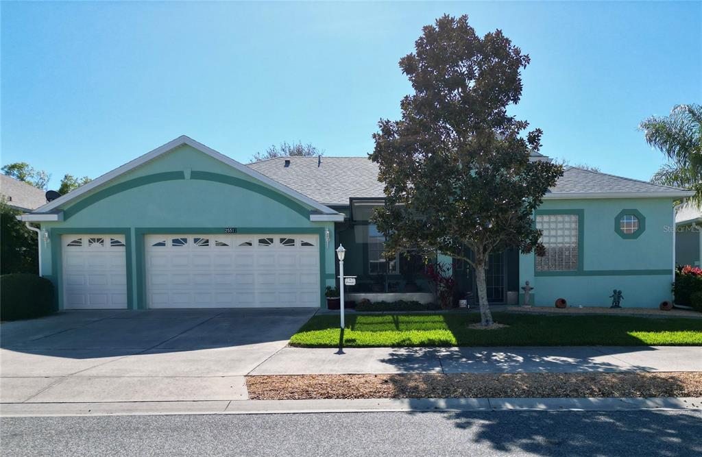 A single-story house with a light green exterior, a three-car garage, and a large tree — 25517 LAUREL VALLEY ROAD, LEESBURG, FL