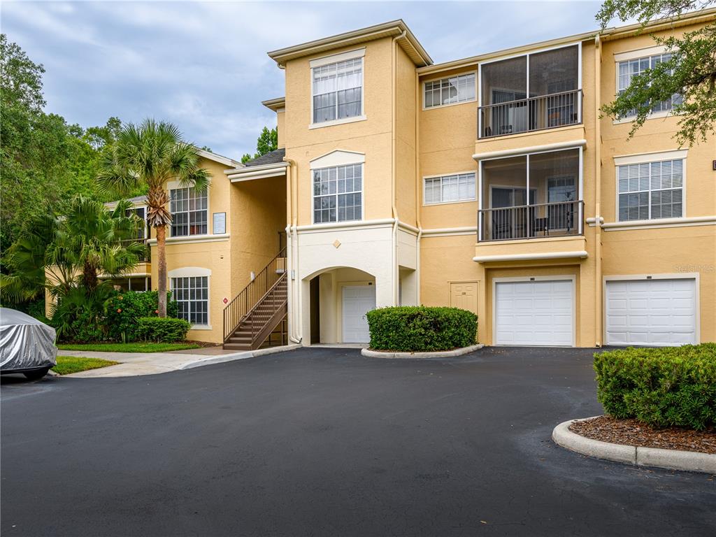 A three-story tan apartment building with screened balconies, stairs, and two ground-level garages — 5125 PALM SPRINGS BOULEVARD UNIT 7108, TAMPA, FL