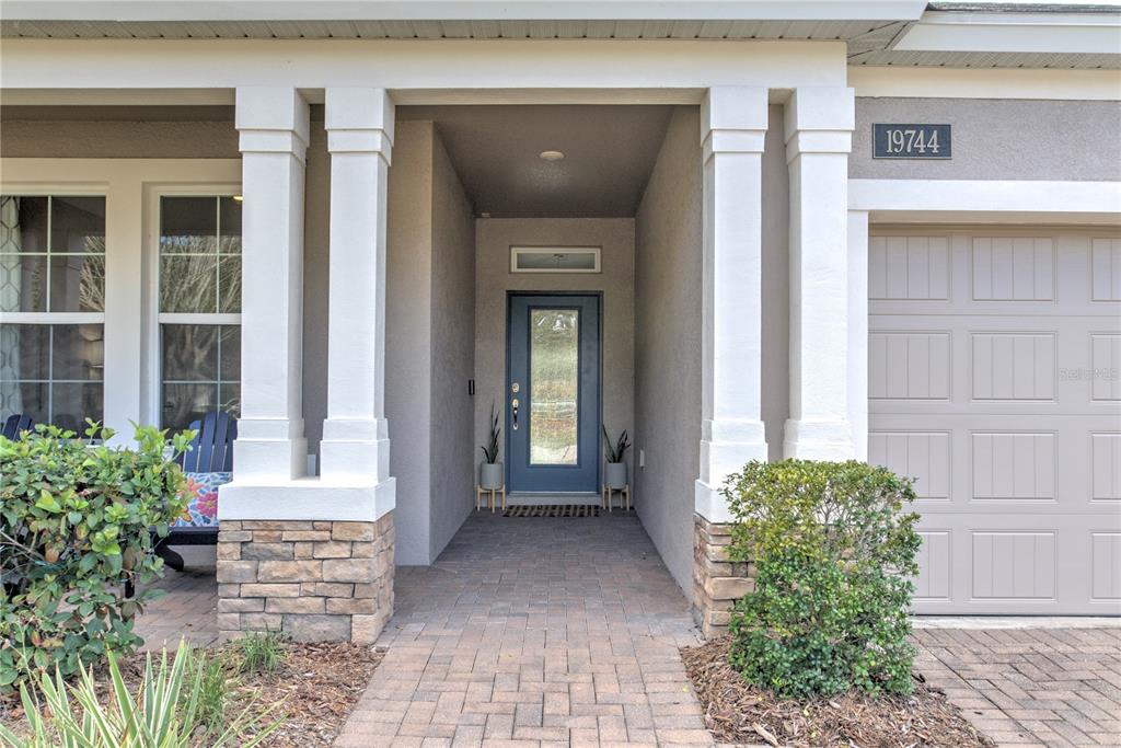 The front exterior features a covered entryway with stone-based columns and a blue front door — 19744 FORT KING RUN, BROOKSVILLE, FL