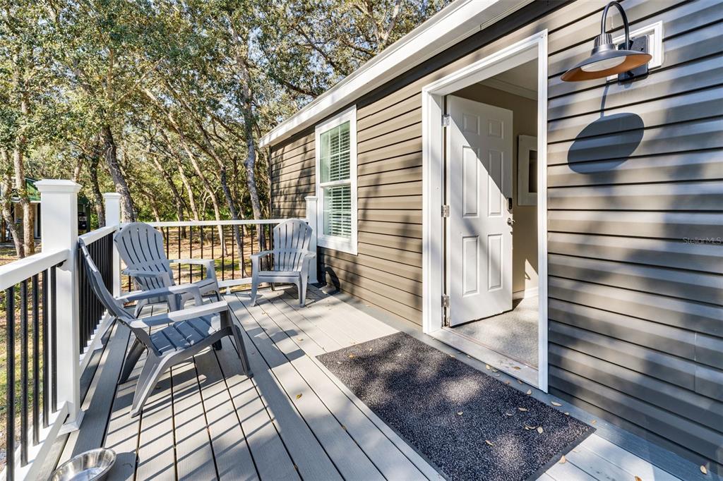 A wooden deck with gray chairs sits outside a house with dark horizontal siding — 8125 SHELLEY TRAIL, KISSIMMEE, FL