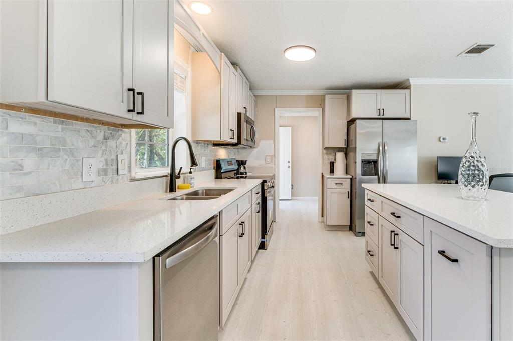 A modern kitchen features white cabinetry, quartz countertops, stainless steel appliances, and a marble backsplash — 8125 SHELLEY TRAIL, KISSIMMEE, FL