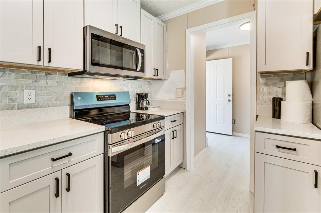 A kitchen features white cabinets, stainless steel appliances, a tiled backsplash, and light-colored countertops — 8125 SHELLEY TRAIL, KISSIMMEE, FL