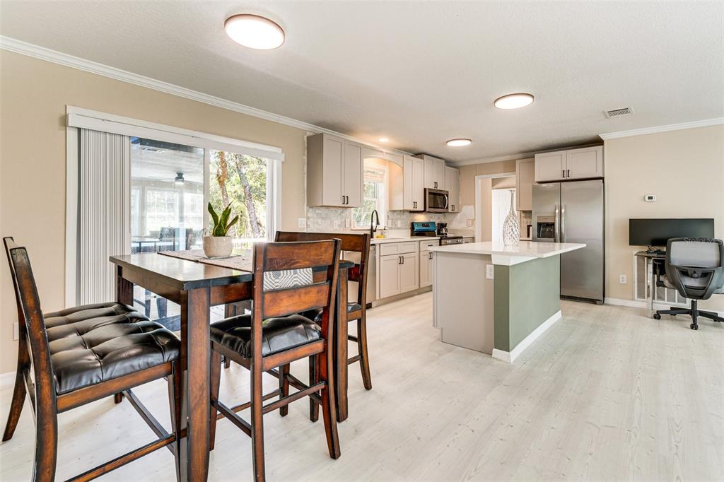 A kitchen and dining area with light wood flooring, gray cabinets, and a kitchen island — 8125 SHELLEY TRAIL, KISSIMMEE, FL