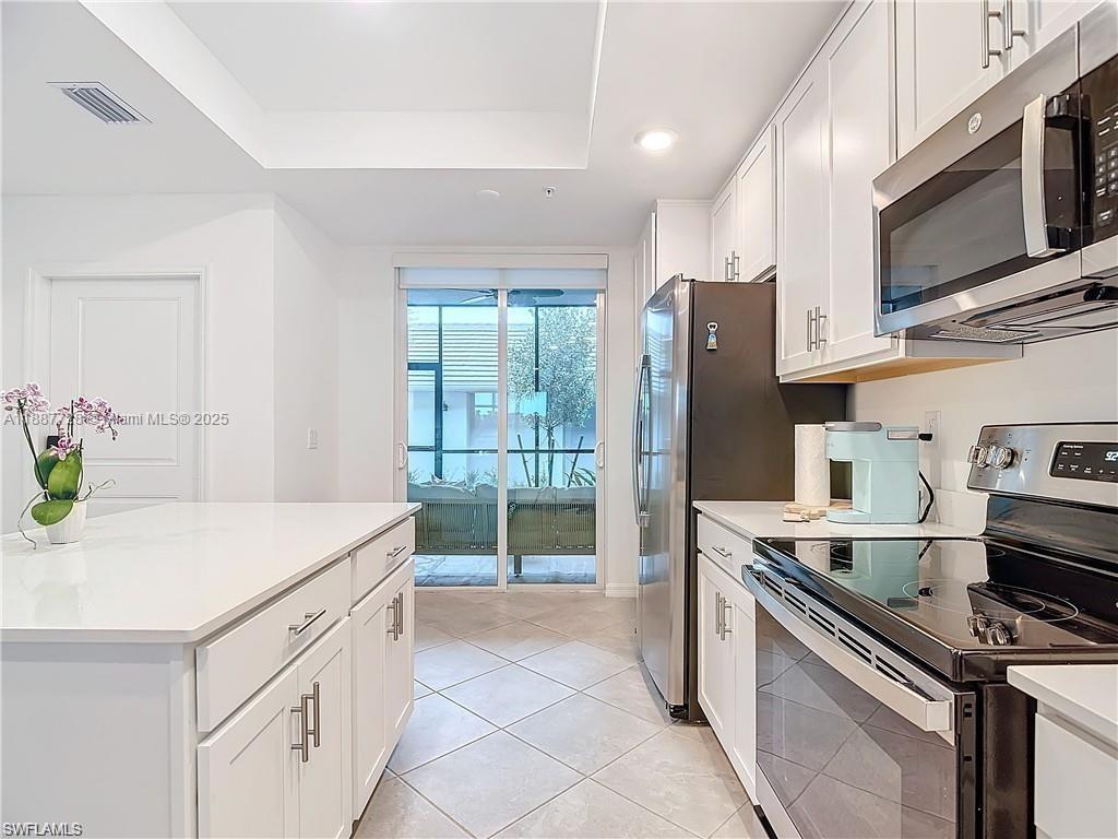 A modern kitchen features white cabinets, stainless steel appliances, a center island, and sliding glass doors — 5453 Double Eagle Cir #3115, Ave Maria FL 34142, AVE MARIA, FL