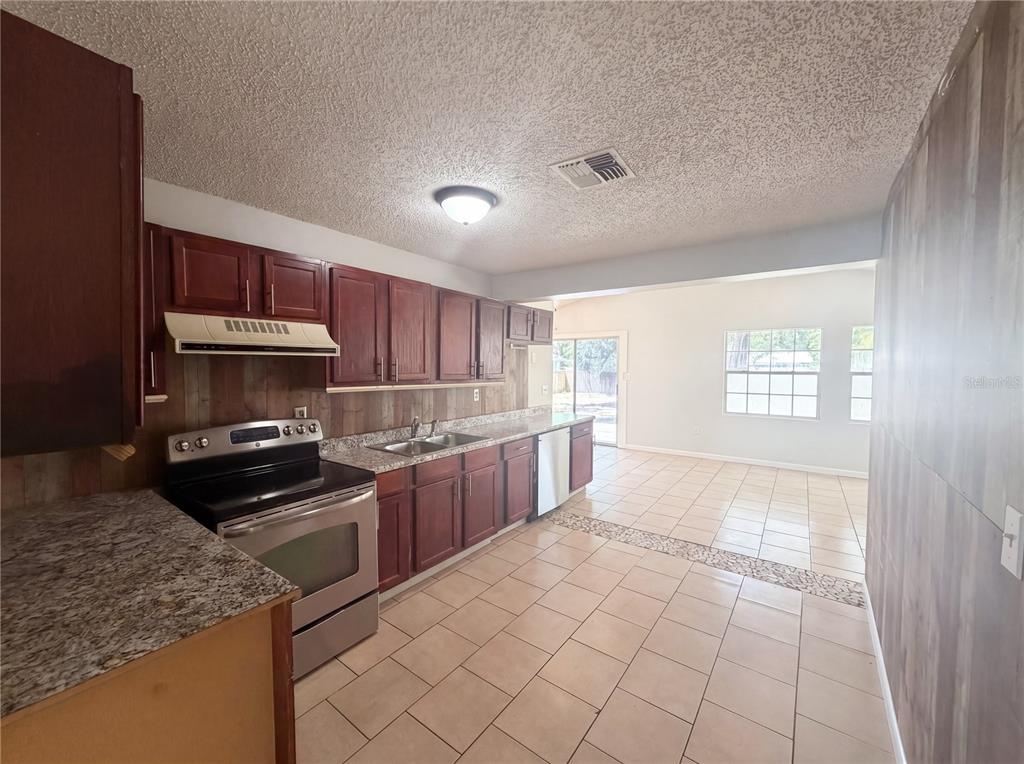 A kitchen with dark wood cabinets, granite countertops, and tile flooring opens to a living area — 613 4TH STREET NE, FORT MEADE, FL