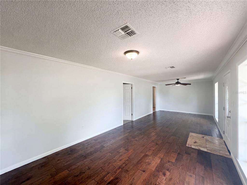 An empty living room features dark wood flooring, white walls, a ceiling fan, and a door — 613 4TH STREET NE, FORT MEADE, FL