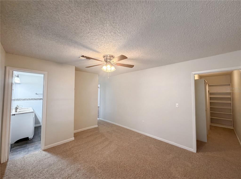 A carpeted bedroom features a ceiling fan, an attached bathroom, and a walk-in closet — 613 4TH STREET NE, FORT MEADE, FL