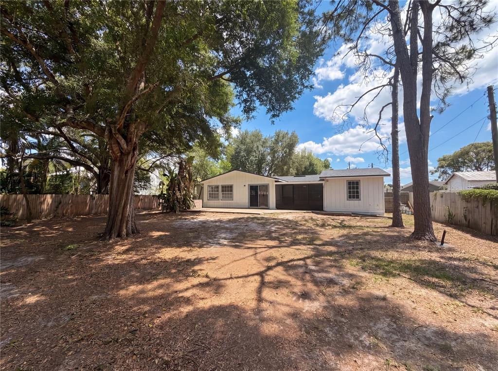 The backyard of a single-story house features a patio, screened porch, and large shade trees — 613 4TH STREET NE, FORT MEADE, FL
