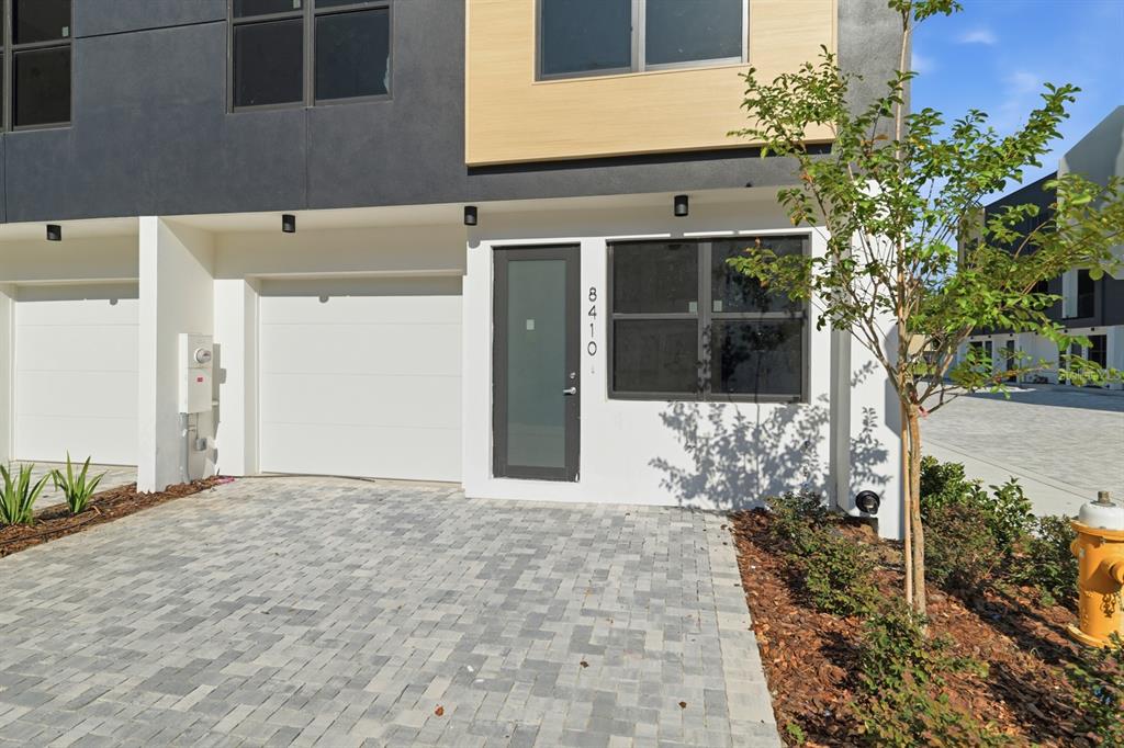 A modern two-story townhouse exterior features a white garage, a glass front door, and pavers — 8401 MODANO PLACE, TAMPA, FL