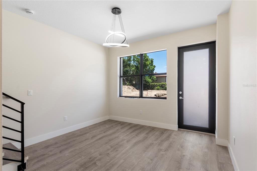 An empty room features light-colored walls, wood-look flooring, a modern pendant light, and a glass-paneled door — 8401 MODANO PLACE, TAMPA, FL