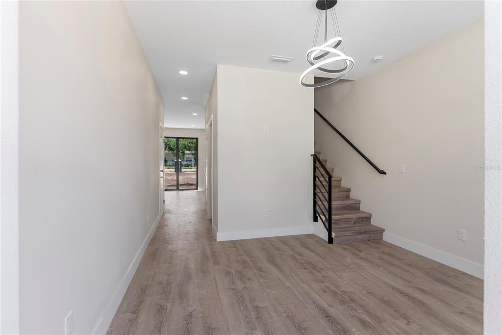 An interior view shows a room with wood-look flooring, a staircase, and a modern chandelier — 8401 MODANO PLACE, TAMPA, FL