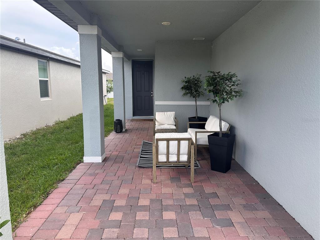 A covered patio features paver flooring, a dark front door, and outdoor seating furniture — 3864 GIORGIO DRIVE, WINTER HAVEN, FL
