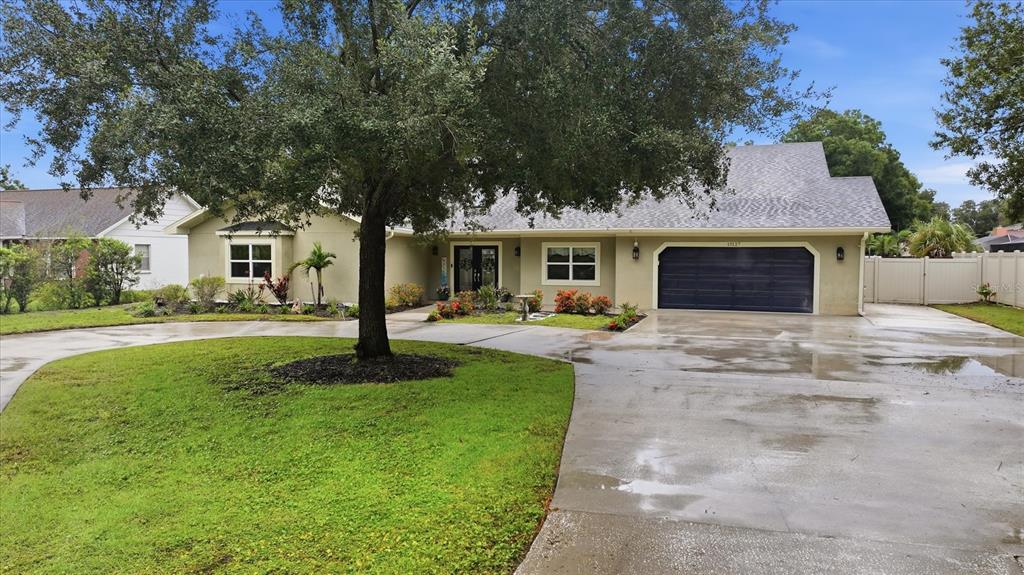 A single-story house with a large tree, a concrete driveway, and a dark garage door — 15127 PENNINGTON ROAD, TAMPA, FL