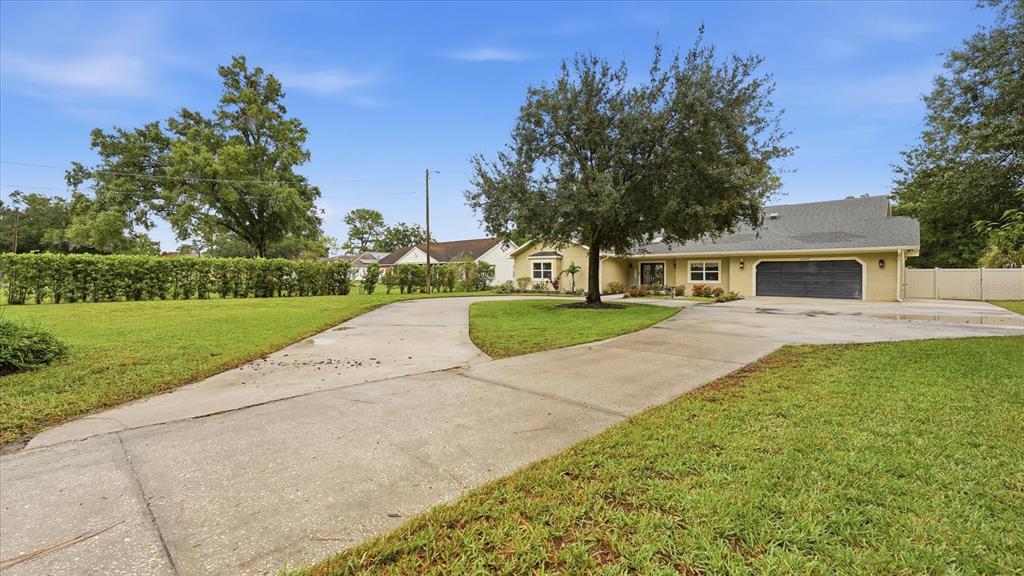 A single-story house with a large concrete driveway, a prominent tree, and a two-car garage — 15127 PENNINGTON ROAD, TAMPA, FL