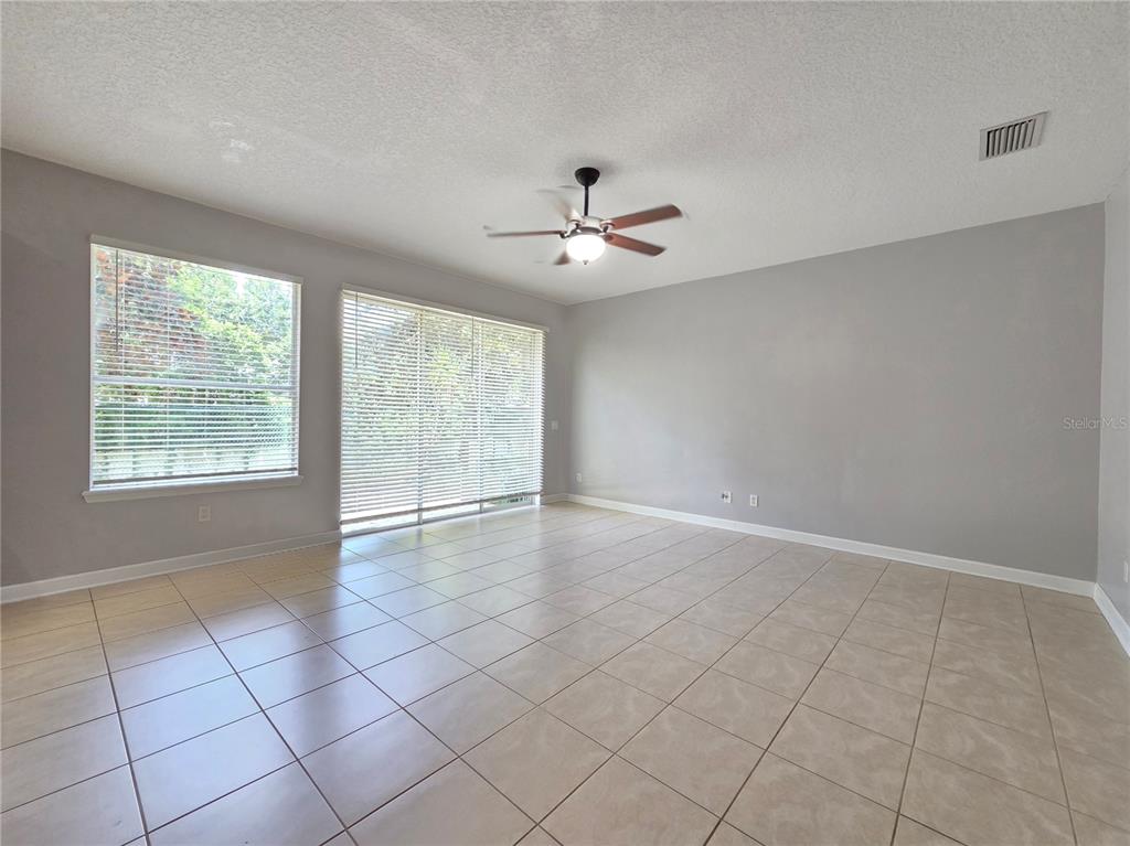 A living room features light-colored tile flooring, gray walls, a ceiling fan, and large windows — 337 CORAL BEACH CIRCLE, CASSELBERRY, FL