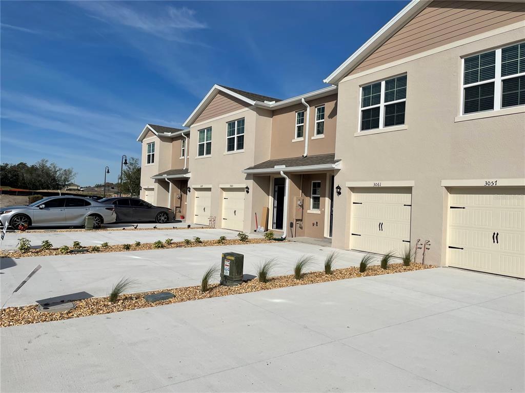 A row of multi-story townhouses with beige stucco exteriors and attached garages under a blue sky — 3057 CANARY AVENUE, DAVENPORT, FL