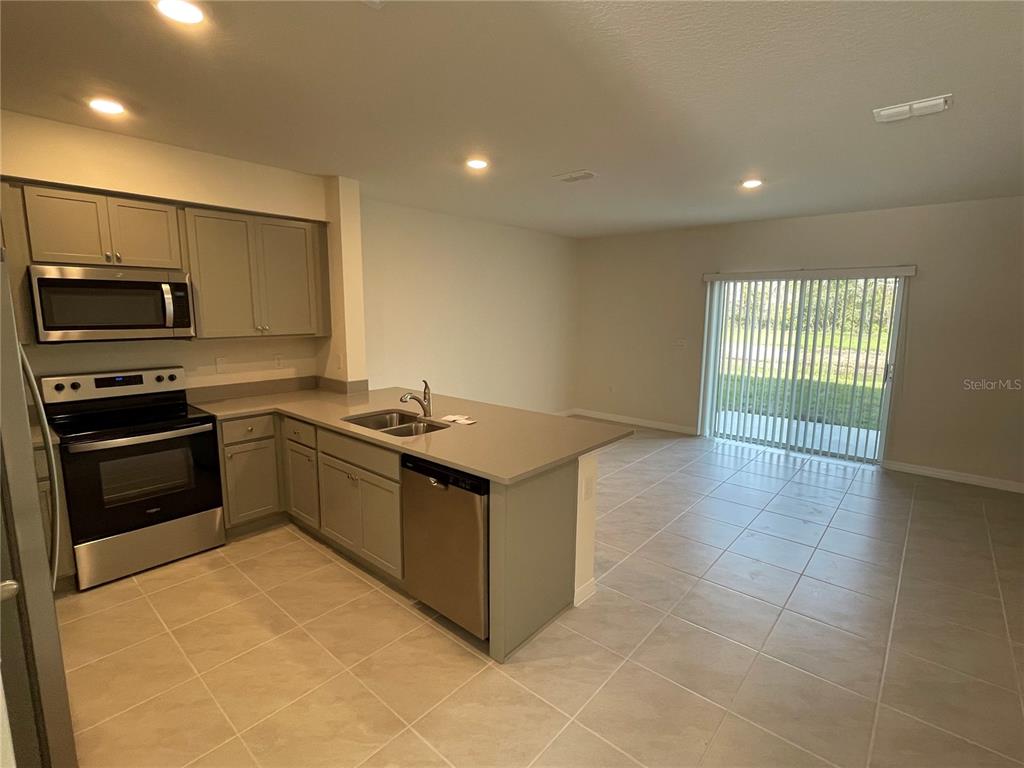 A kitchen with stainless steel appliances and light-colored cabinets opens to a tiled living area — 3057 CANARY AVENUE, DAVENPORT, FL