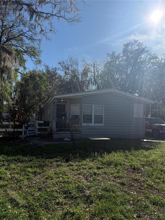 A single-story house with gray siding sits on a grassy lot under large trees — 8602 TREASURE ISLAND ROAD, LEESBURG, FL