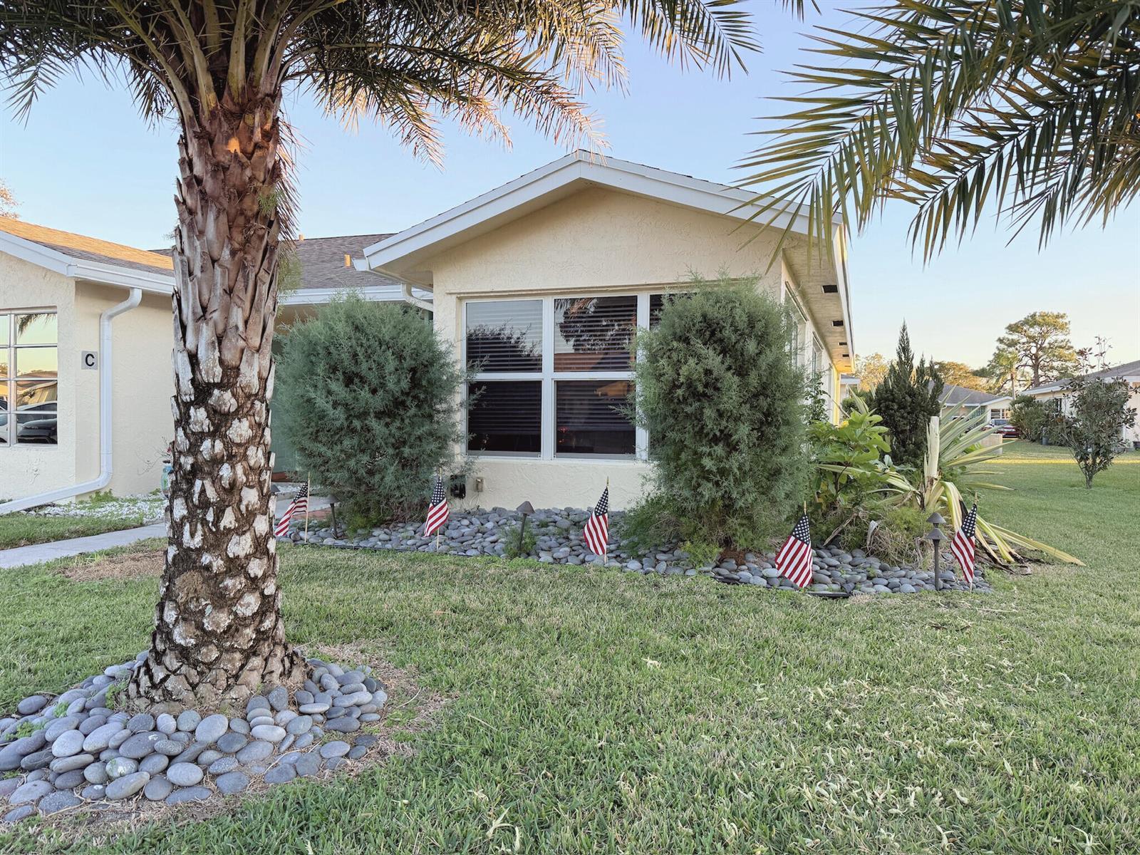 A single-story house exterior features a palm tree, rock landscaping, and small American flags — 5301 Lakefront Boulevard # D, Delray Beach FL 33484, DELRAY BEACH, FL
