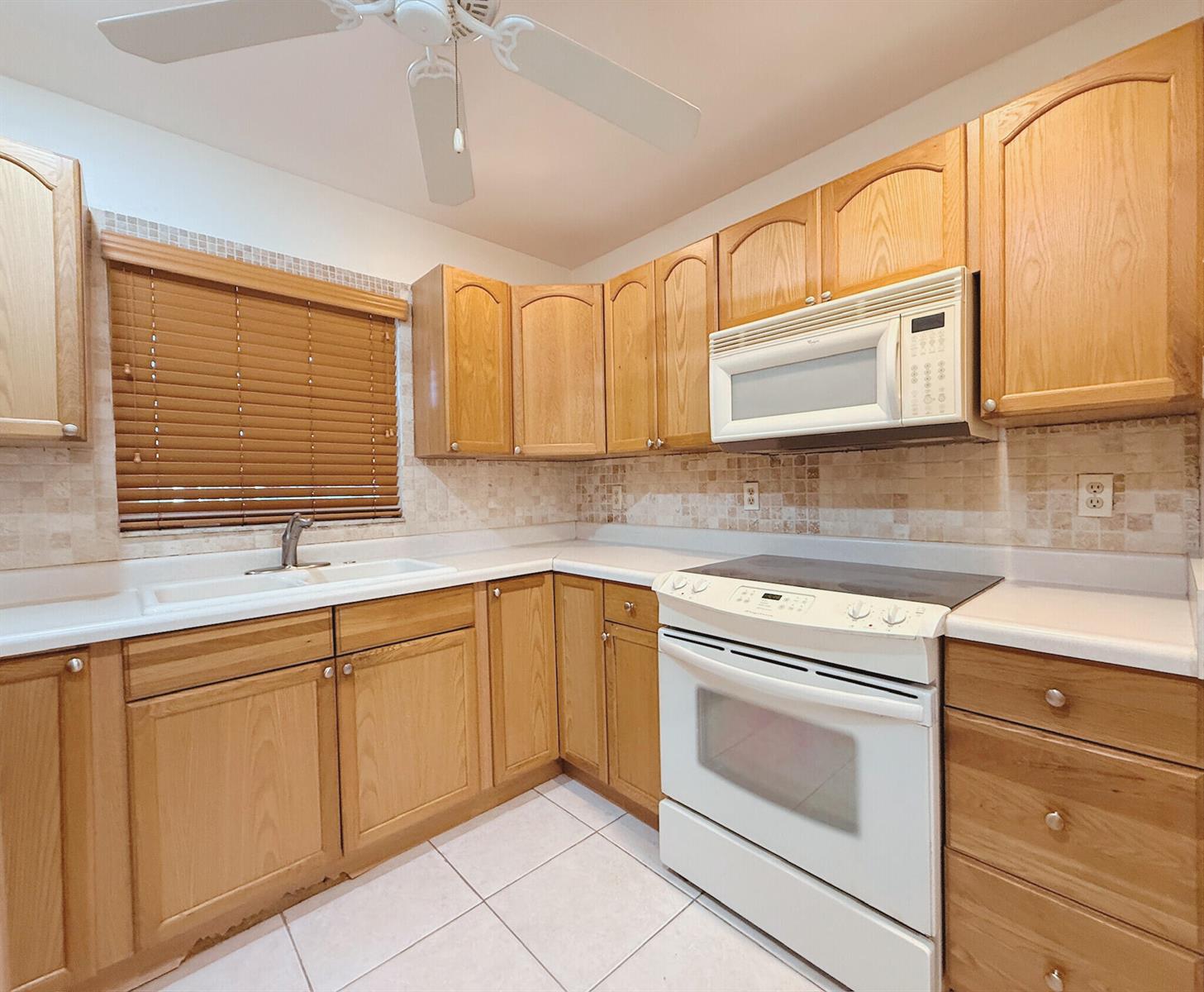 A kitchen features light wood cabinets, white appliances, a tiled backsplash, and a ceiling fan — 5301 Lakefront Boulevard # D, Delray Beach FL 33484, DELRAY BEACH, FL