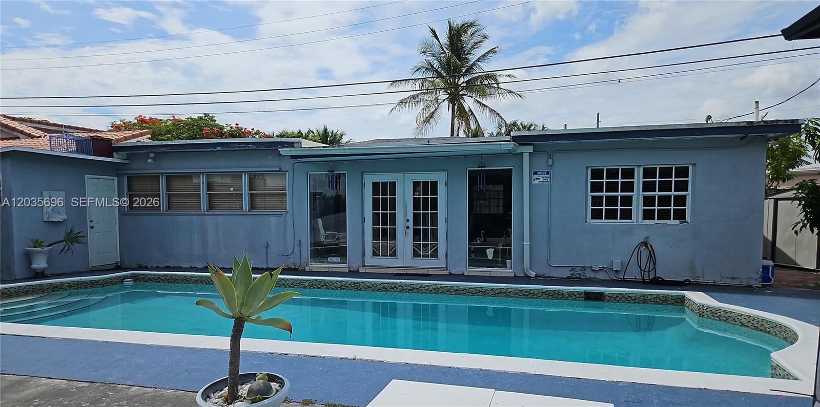 A swimming pool sits in front of a blue house with a palm tree — 6895 Tamiami Canal Rd, Miami FL 33126, MIAMI, FL
