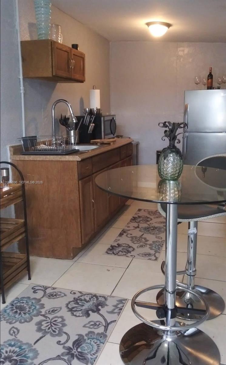 A small kitchen features wooden cabinets, a glass-topped table, and a stainless steel refrigerator — 6895 Tamiami Canal Rd, Miami FL 33126, MIAMI, FL